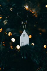 White ceramic house shaped ornament on a green Christmas tree background.