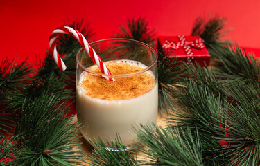 Glass of eggnog with pine needles, one small present box on a red background