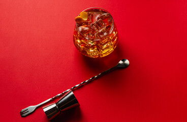 Top angle view of an ice tea with jigger and bar spoon on a red table