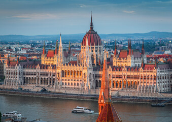 The photo captures the Hungarian Parliament Building in Budapest during sunset, beautifully reflecting the warm sunlight on its Neo-Gothic architecture along the Danube River.