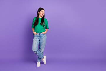 Joyful young woman in casual style with green t-shirt and jeans posing against a vibrant purple background