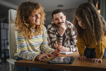 mum, dad and daughter use digital tablet on wooden table