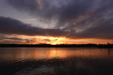 Obraz premium Beautiful natural autumn landscape with dramatic sunset and forest silhouette on horizon against calm river