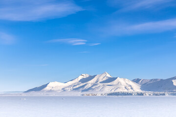 Snow on the fast ice of Svalbard with glacier and mountains and a blue summer sky. Svalbard is Norwegian archipelago between mainland Norway and the North Pole