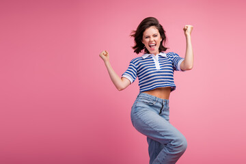 Naklejka premium Young woman exuding happiness on pink background, stylish in striped polo and jeans