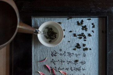 Top view image of a scene of a cup of oolong tea being poured from an old teapot on to a textured...
