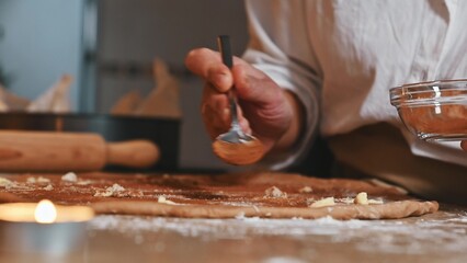 Baker speading butter and spices on rolled dough in a cozy, candle-lit kitchen