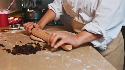 Baker rolling dough with raisins on a table in a cozy kitchen