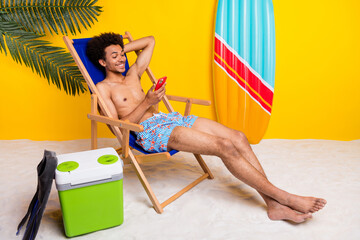 Young man relaxing on a beach chair with a cheerful yellow background, enjoying a sunny day with surfboard and cooler nearby