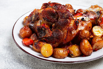 Pork knuckle baked with vegetables, new potatoes , on a white plate, homemade, no people,