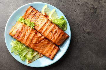 Delicious grilled salmon fillets with lettuce and lemon on grey table, top view. Space for text