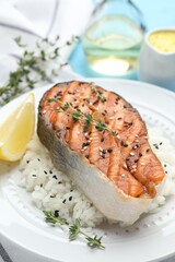 Tasty grilled salmon steak with rice, thyme, lemon and sesame seeds on table, closeup