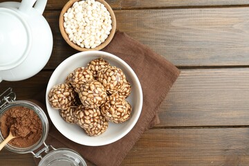 Tasty chocolate puffed rice balls, ingredients and teapot on wooden table, flat lay. Space for text