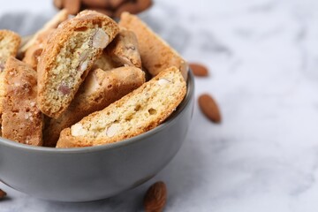 Tasty almond biscuits (Cantuccini) in bowl and nuts on light table, closeup. Space for text