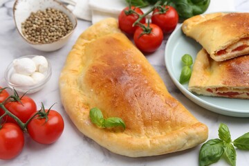 Tasty vegetarian calzones with tomatoes, mozzarella cheese and spices on white marble table, closeup