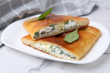 Pieces of tasty calzone with cheese and basil on white marble table, closeup