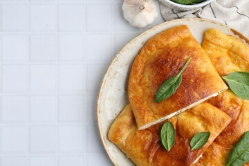 Tasty calzones with basil and cheese on white tiled table, top view. Space for text