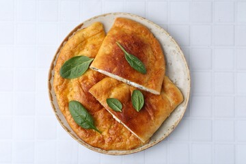Tasty calzones with basil and cheese on white tiled table, top view