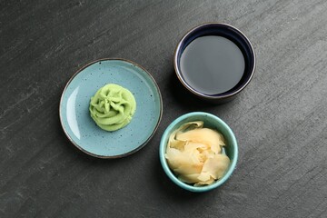 Hot wasabi paste, soy sauce and ginger on dark textured table, flat lay