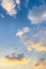 A bright sky at sunrise or sunset, with soft gradients of blue mixed with gold and orange, as clouds spread out, some illuminated by sunlight.