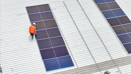 Aerial view of a rooftop with solar panels, showing a technician in safety gear performing maintenance. The scene highlights renewable energy, solar technology, and sustainable infrastructure.