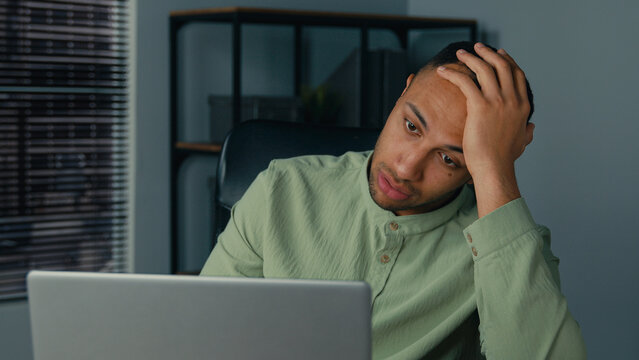 Desperate frustrated stressed african american man receive bad news by email on laptop in office evening sad worried shocked male businessman employee browsing computer crash error problem fail online