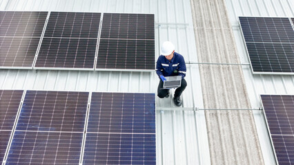 technician in hard hat and safety gear inspects solar panels on a metal rooftop, holding a tool....