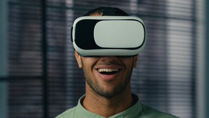 Close-up smiling latin american man wearing virtual reality glasses friendly showing invitation gesture asking to come welcome symbol making choice male player playing in cyberspace with vr goggles