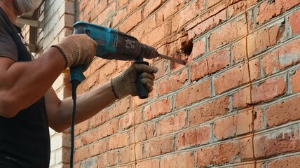 a hard worker in a black T-shirt and a blue protective mask with a pneumatic hammer hammering a red...