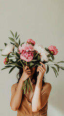 Woman holds a bouquet of peonies in her hands covering her face. Space for text. Pastel palette. Greeting card