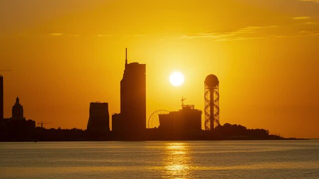 Sunset sun sets behind silhouette of city of Batumi on sea coast, day night timelapse.