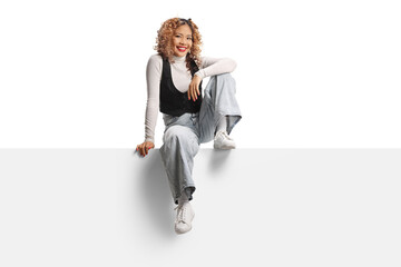 Cheerful young asian woman with curly hair sitting on a blank panel