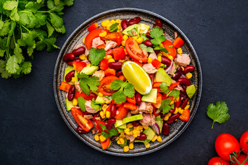 Mexican style salad with tuna, avocado, corn, beans, tomatoes and cilantro, black background, top view
