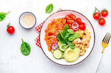 Salad bowl with salmon, shrimps, avocado, spinach, vegetables, sesame and cashew nuts for keto diet. White background, top view