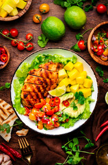 Foodie food salad bowl with grilled chicken and mango, tomato, cilantro, onion, salsa and lettuce wood background, top view