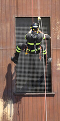 firefighter wearing a uniform and climbing harness scales the side of a building using safety ropes...