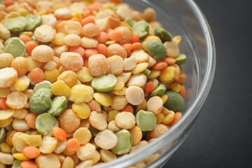 Various colorful split legumes in a glass bowl on a black background. (peas, lentils). Close up.