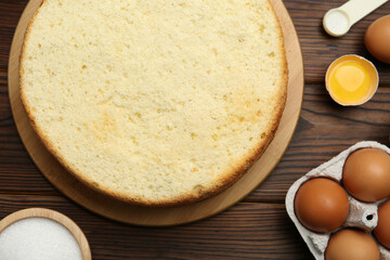 Delicious cut sponge cake and ingredients on wooden table, flat lay