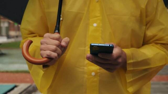 Using phone taxi app during rain, Unrecognizable man standing on the city streets under umbrella and using cellphone
