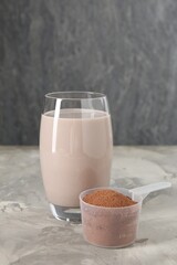 Delicious protein shake in glass and scoop with powder on grey table