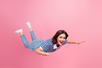 Young woman in a casual outfit floating joyfully against a pink backdrop, expressing a sense of...