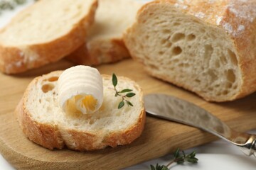 Cut baguette with butter and herbs on white wooden table, closeup