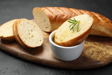 Cut fresh baguette with balsamic and rosemary on black table, closeup