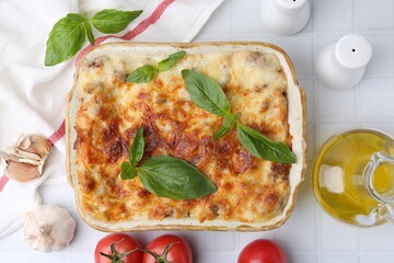 Delicious cooked lasagna with basil served on white tiled table, flat lay