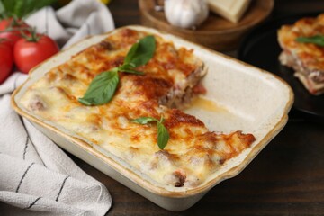 Delicious cooked lasagna with basil in baking dish on wooden table, closeup