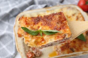 Taking piece of delicious cooked lasagna with basil at table, closeup