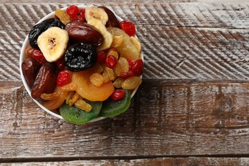 Mix of different dried fruits in bowl on wooden table, top view. Space for text
