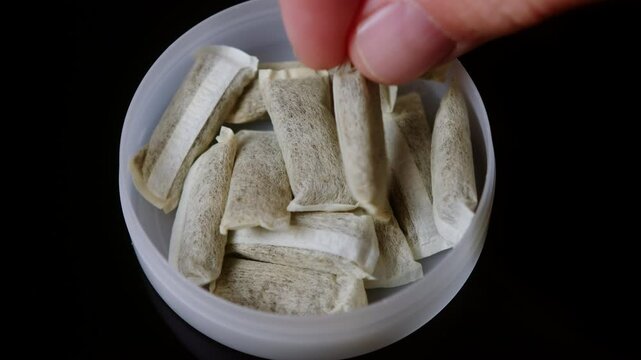 Snus nicotine tobacco close up, pack of tobacco for gum. unhealthy addiction. Man opening box with snus and taking one. 
