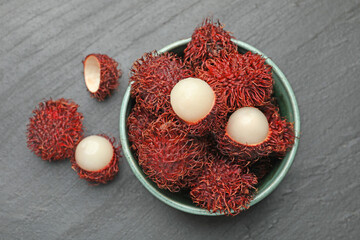 Delicious ripe rambutans in bowl on black table, top view