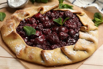 Tasty galette with cherries, mint and powdered sugar on wooden table, closeup